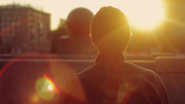 Parte posteriore dell'uomo in giacca di pelle sedersi sulla panchina in raggi di sole in città. Goditi il tramonto rosso. Attività ricreative — Video Stock