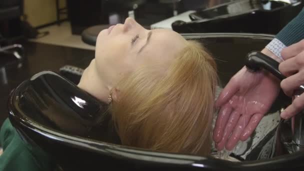 Professional barber tune water to wash hair of blonde young girl in beauty saloon. Hair care — Stock Video