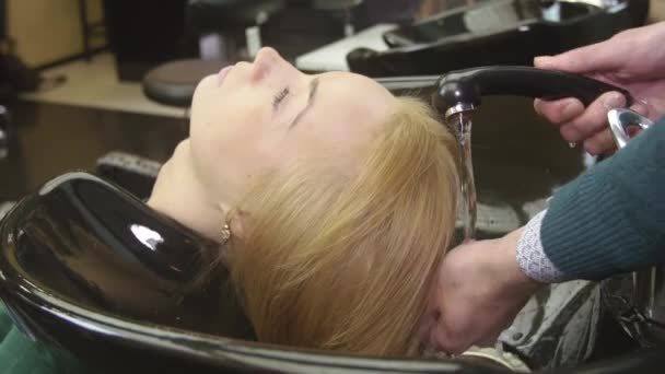 Professional hairdresser washing hair of blonde young girl in beauty saloon. Hair care. Barbershop — Stock Video