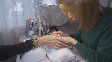 Manikürcü turuncu sopa ile güzellik salonu kadının tırnaklarından shellac kapak koydu. Düzeltme