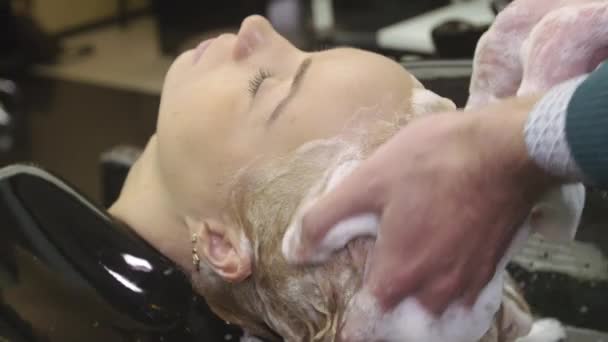 El peluquero profesional frotan en el champú en los cabellos de la muchacha rubia joven en la barbería. Masaje de cabeza — Vídeos de Stock