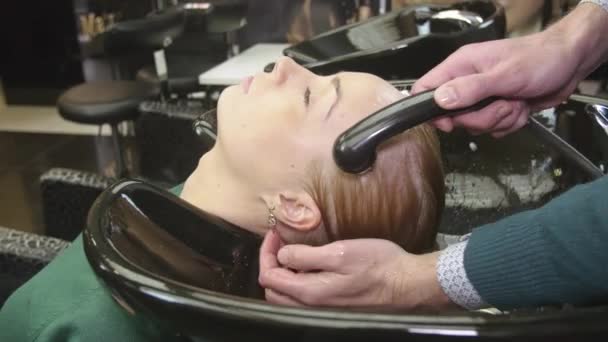 Professional barber wash hair of blonde girl by water in beauty saloon. Massage of head. Hair care — Stock Video