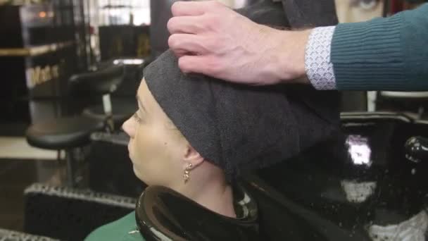 Cabeleireiro profissional põem o cabelo da menina loira pela água na toalha no salão de beleza. Cuidados com o cabelo — Vídeo de Stock