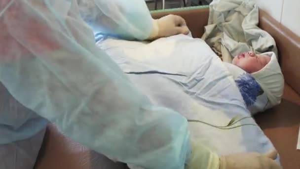 Медсестра в перчатках пеленает новорожденного ребенка после рождения на столе в синем одеяле. Родильный дом . — стоковое видео