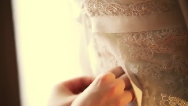 Frau binden Bänder auf der Rückseite des Brautkleides mit Spitze an Braut. Feiertag. Ehe. warme Farbtöne. — Stockvideo