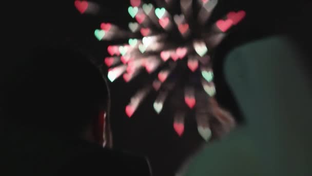 La parte posteriore di coppia nuziale di sagoma guarda a fuochi d'artificio in cielo di notte nella forma di cuori. Abbracciare — Video Stock