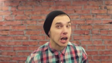 Siyah şapkalı ekose gömlek genç blogger kamera kelimeleri telaffuz, gül. Arka plan üzerinde tuğla duvar.