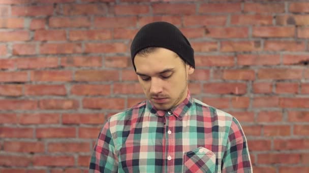 Blogger in black hat, plaid shirt speak words in camera with sad face. Brick wall on background. — Stock Video