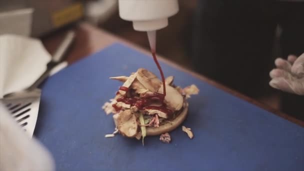 Kucharz w rękawice wlać ketchup na przygotowane hamburger z mięsem. Fast food. Letni dzień. Zdarzenie open air — Wideo stockowe
