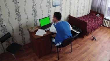 Defter yurt odasında oturan genç adam. Eski yatak kırmızı battaniye ile. Synthesizer. Öğrenci