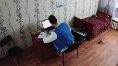 Defter yurt odasında oturan çocuk. Eski yatak kırmızı battaniye ile. Telefonu al. Öğrenci