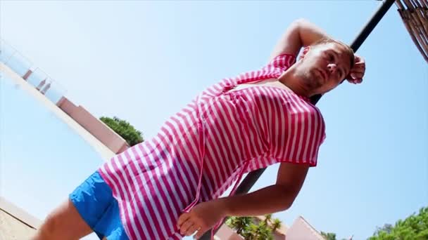 セクシーなピンクのチュニックに男ポーズ見てカメラでビーチ パラソル。風。夏の晴れた日。青い空 — ストック動画