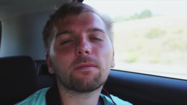 Hombre barbudo joven mostrar la lengua en la cámara con los ojos cerrados dentro del coche de conducción. Viento. Abrir ventana . — Vídeos de Stock