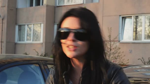 Brunette girl in sunglasses sing in camera, wave head at house on street in summer sunny evening. — Stock Video