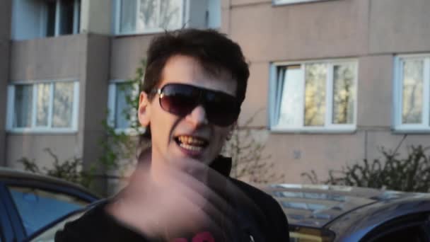 Brunette man in sunglasses read rap in camera on street in summer evening. Black jacket. Gesture — Stock Video