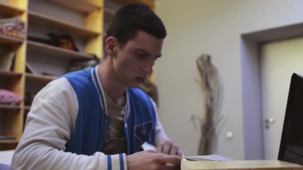 Le jeune garçon en veste regarde sur des feuilles de papier, s'assoit volontiers sur une chaise et s'étire. Étudiant 