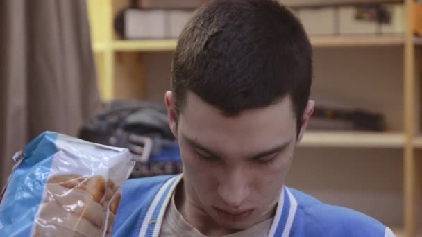 Porträtt av klumpig brunette pojke äta chips framför skärmen av anteckningsboken i rummet. Sömnig. Trötthet. — Stockvideo