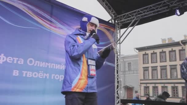 Sint-Petersburg, Rusland - 27 oktober 2013: Jonge man host in paars jasje, warme muts met microfoon op het podium. Concert. Evenement. — Stockvideo