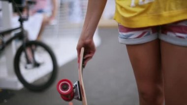 Şortlu genç kadın elinde kaykay kırmızı tekerlekler ile bükmek. Yaz gecesi. Parlak tırnaklar