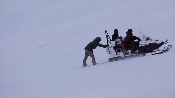 Snowboarder κρατήστε οδήγηση του snowmobile στην χιονισμένη πλαγιά στο βουνό. Οι άνθρωποι. Ψυχαγωγία. Διασκέδαση — Αρχείο Βίντεο