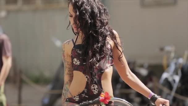 MOSCÚ, RUSIA - 27 de julio de 2015: Sexy chica tatuada de cabello oscuro en traje de baño negro posando sobre una bicicleta verde pintada. Día soleado de verano . — Vídeo de stock
