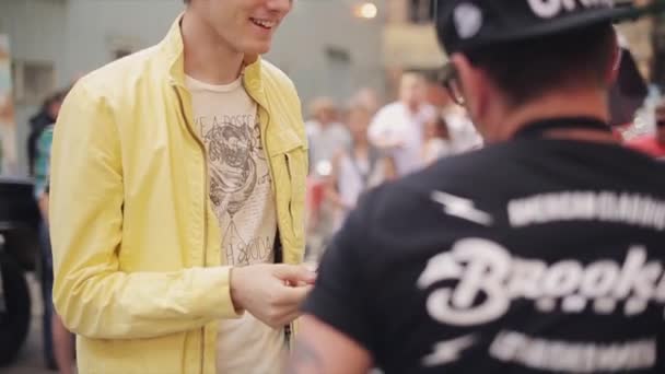 Μόσχα, Ρωσία-27 Ιουλίου, 2015: νέος άντρας με γυαλιά ηλίου, κίτρινο μπουφάν έρχεται να φιλοξενήσει με μικρόφωνο του δώσει κάρτα. Καλοκαίρι. Λαχείο — Αρχείο Βίντεο
