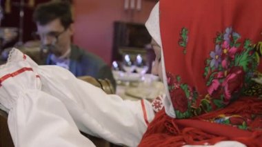 Woman in red shawl on head, Russian national clothes sitting at table. Flirting with man in glasses