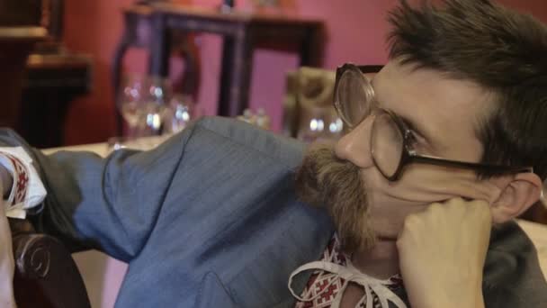 Man in glazen met snor in Russische nationale kleren zitten aan tafel krijgt klap in het gezicht — Stockvideo