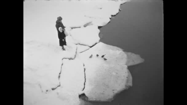 El hombre con sombrero de piel se queda en la nieve en el río con una niña alimentando palomas en el témpano de hielo. El invierno. Agua. — Vídeos de Stock