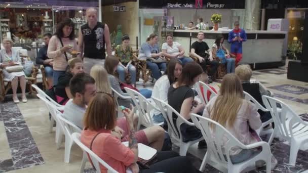 СЕНТ-ПЕТЕРБУРГ, РОССИЯ - 4 ИЮНЯ 2016: Многие люди сидят на стульях в зале торгового центра. Посетители мероприятия. Солнце — стоковое видео