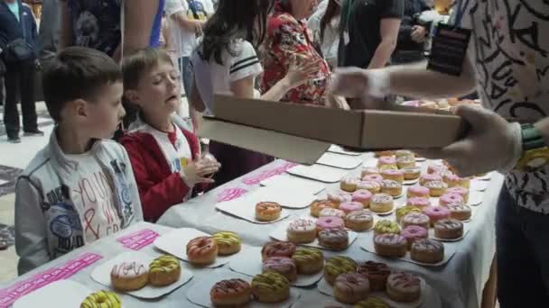 SAINT PETERSBURG, RÚSSIA - JUNHO 4, 2016: O homem colocou donuts coloridos na mesa no centro comercial. É justo. Gente. Crianças. — Vídeo de Stock