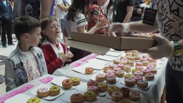 SAINT PETERSBURG, RUSSIA - JUNE 4, 2016: Man put colorful doughnuts on table in shopping center. Fair. People. Children — Stock Video