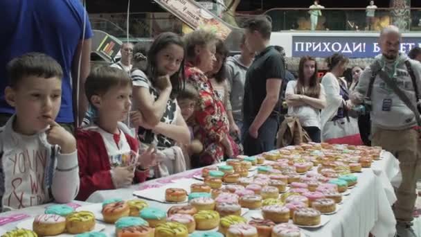 サンクトペテルブルク, ロシア連邦 - 2016 年 6 月 4 日: 女の子は、ショッピング センター内のテーブルにカラフルなドーナツを置きます。公正です。待機児童 — ストック動画