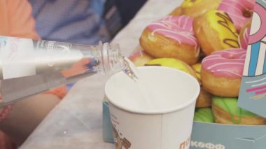 Saint Petersburg, Rusya - 4 Haziran 2016: Kadın masaya sırla kaplı birçok donutla cam, kutuya su döküyor