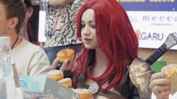 Sankt Petersburg, Ryssland-4 juni 2016: Röd hår flicka i anime Suit ät munkar vid bordet på Speed. Tävling. Människor. — Stockvideo