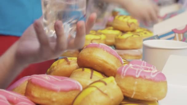 SAINT PETERSBURG, RÚSSIA - JUNHO 4, 2016: Mulher fechar garrafa com água, caixa com muitos donuts cobertos por esmalte na mesa — Vídeo de Stock