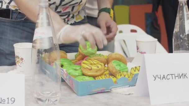 СЕНТ-ПЕТЕРБУРГ, РОССИЯ - 4 ИЮНЯ 2016: Человек в перчатках считает пончики, покрытые глазурью в коробке. Конкурс. Задача . — стоковое видео
