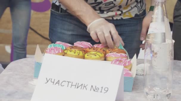 SAN PETERSBURG, RUSIA - 4 DE JUNIO DE 2016: El hombre con guantes cuenta coloridas rosquillas cubiertas de esmalte en caja. Concurso. Gente — Vídeos de Stock