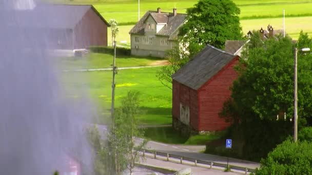 Wasserfall plätschert vor der Kamera. Blick auf kleine Holzhäuser. Sommersonniger Tag. grünes Gras — Stockvideo