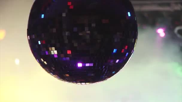 La bola de discoteca giratoria refleja vigas de colores brillantes de focos en la discoteca. Fuma. Vacaciones — Vídeo de stock