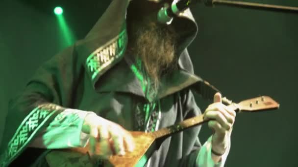 SAINT PETERSBURG, RUSSIA - JUNE 26, 2015: Bearded vocalist in mantle play balalaika on stage in nightclub. Green spotlights. Entertainment — Wideo stockowe