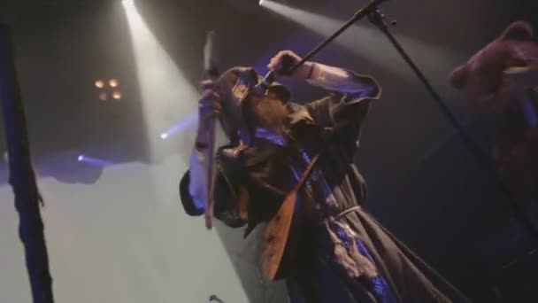 SAINT PETERSBURG, RUSSIA - JUNE 26, 2015: Bearded vocalist in mantle with balalaika, axe on stage in nightclub. Spotlights. Live performance — стокове відео