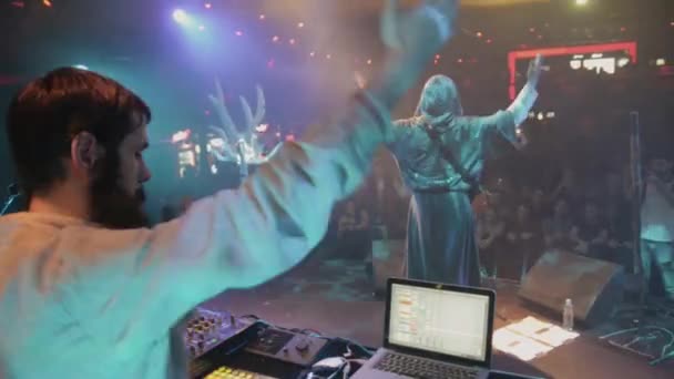 SAINT PETERSBURG, RUSIA - 26 DE JUNIO DE 2015: Vocalista en el manto, DJ en ropa folclórica agita las manos en el escenario en la discoteca. Proyectores azules . — Vídeos de Stock