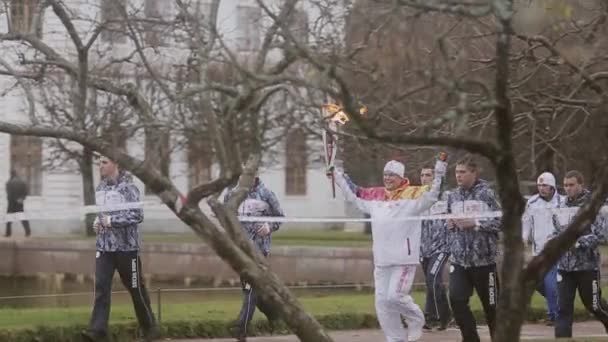 SAINT PETERSBURG, RUSSIA - OCTOBER 27, 2013: Relay race Olympic flame in Peterhof, Saint Petersburg. Torchbearer run with flame, fencing tape — Stock Video