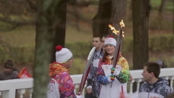 САЙНТ-ПЕТЕРБУРГ, РОССИЯ - 27 октября 2013 года: Эстафета Олимпийского огня в Петергофе, Санкт-Петербург. Женщина-факелоносец пропускает огонь в парке — стоковое видео