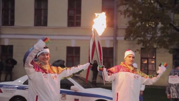 SAN PETERSBURG, RUSIA - 27 DE OCTUBRE DE 2013: Carrera de relevos Llama olímpica en San Petersburgo. El portador de la antorcha pasa la llama a otro hombre. Buenas tardes. Policía. — Vídeo de stock