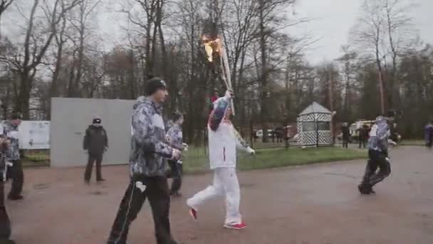 SAN PETERSBURG, RUSIA - 27 DE OCTUBRE DE 2013: Carrera de relevos Llama olímpica en San Petersburgo. El portador de la antorcha funciona con llama en la carretera. Lluvia. Cortejo. — Vídeos de Stock