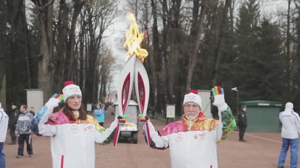 САЙНТ-ПЕТЕРБУРГ, РОССИЯ - 27 октября 2013 года: Эстафета Олимпийского огня в Петергофе, Санкт-Петербург. Пожилой факелоносец передает огонь молодой женщине . — стоковое видео