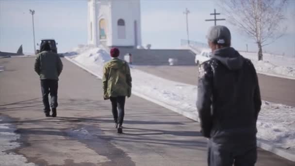 Die Rückseite von drei Männern geht zu einer weißen Kirche mit Goldkuppel. Wintersonniger Tag. Schnee. kalte Schatten — Stockvideo