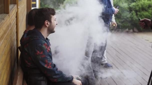 SAN PETERSBURG, RUSIA - 28 DE MAYO DE 2016: La compañía de hombres fuma cigarrillos electrónicos sentados en el banco. Festival de pañales. Vapor — Vídeo de stock